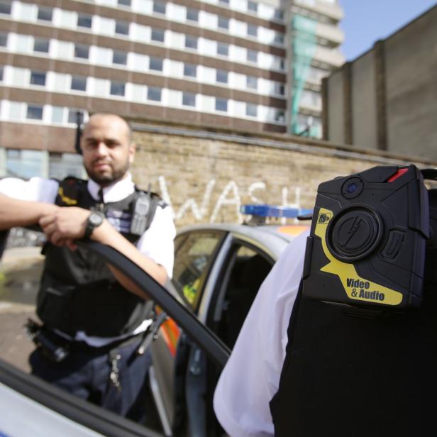 Ein Polizist steht an der offenen Tür eines Streifenwagens, eine Bodycam ist sichtbar.