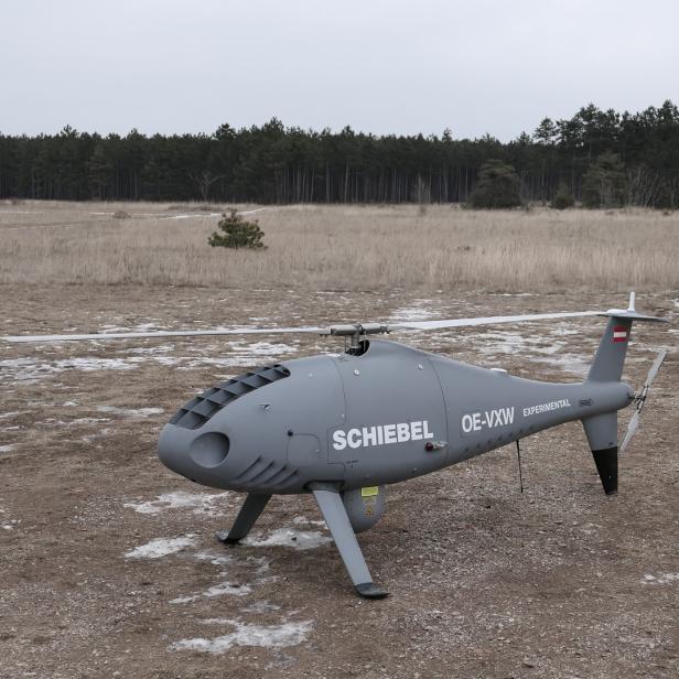 Eine graue Schiebel Camcopter S-100 Drohne steht auf einem Feld.