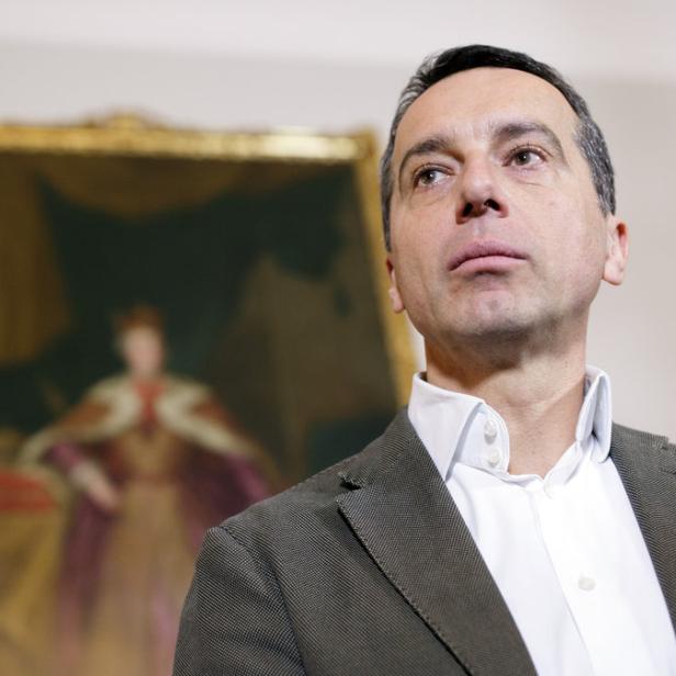 Ein Mann in Jackett und Hemd blickt nach oben, im Hintergrund ein Gemälde.