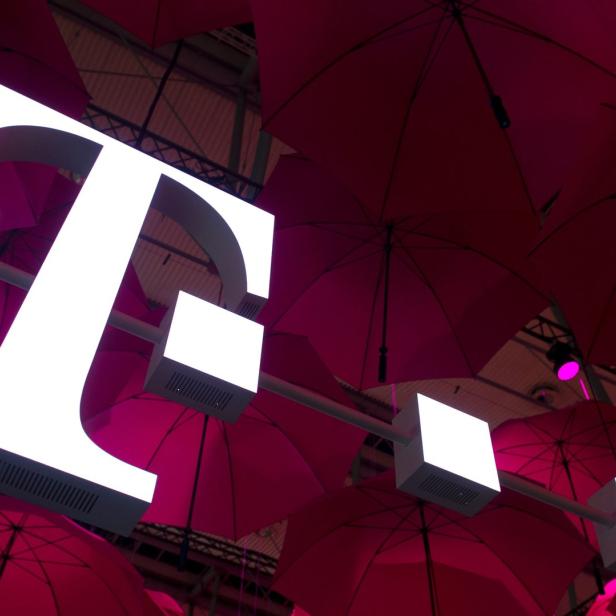 Das beleuchtete „T“-Logo der Telekom vor einem Hintergrund aus roten Regenschirmen.