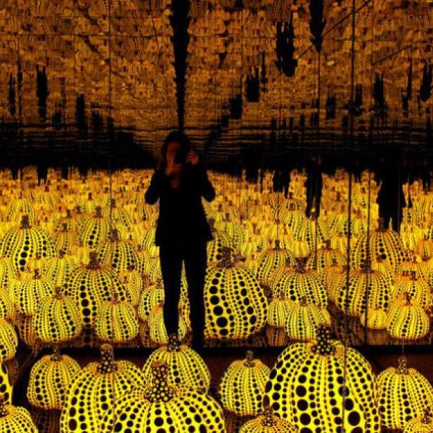 Eine Person steht inmitten einer Installation aus gelben Kürbissen mit schwarzen Punkten.