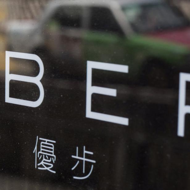 Das Uber-Logo ist auf einer dunklen Oberfläche zu sehen, im Hintergrund ein Taxi.