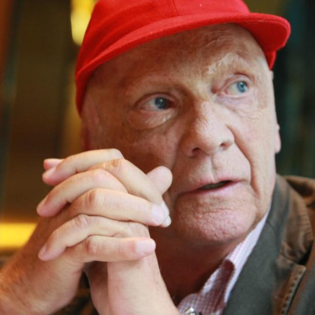 Niki Lauda mit roter Kappe, die Hände vor dem Gesicht verschränkt.