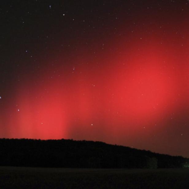 Ein rotes Polarlicht erstreckt sich über eine dunkle Landschaft.