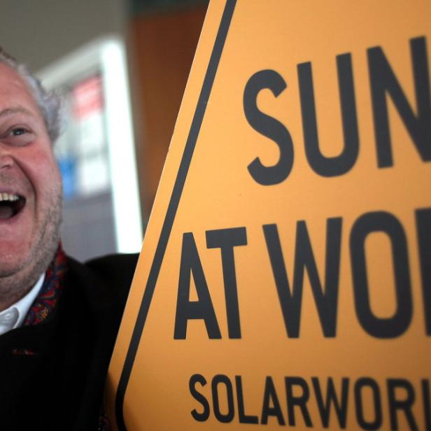 Ein lachender Mann steht neben einem Schild von Solarworld mit der Aufschrift „Sun at Work“.