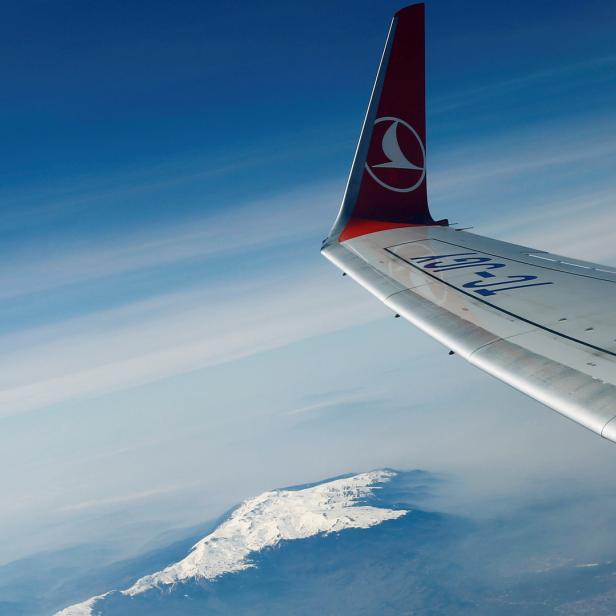 Der Blick aus einem Flugzeugfenster auf ein schneebedecktes Bergmassiv.