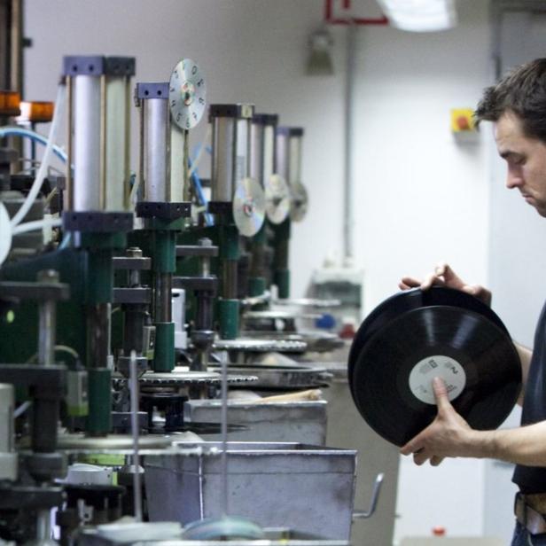 Ein Mann prüft Schallplatten an einer Produktionsmaschine.