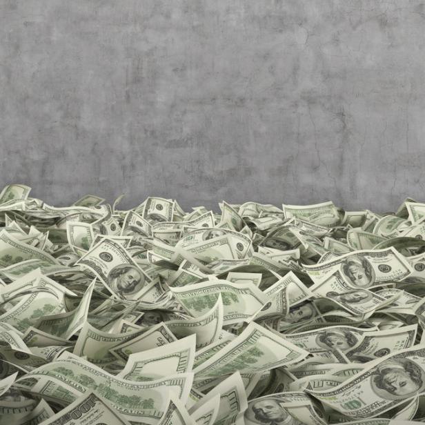 Ein großer Haufen von Hundert-Dollar-Scheinen vor einer grauen Wand.