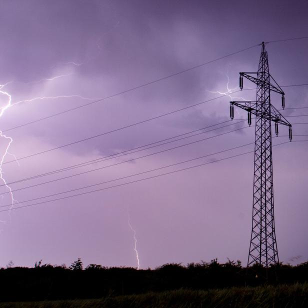 Ein Blitz erhellt den Himmel neben einem Strommast.