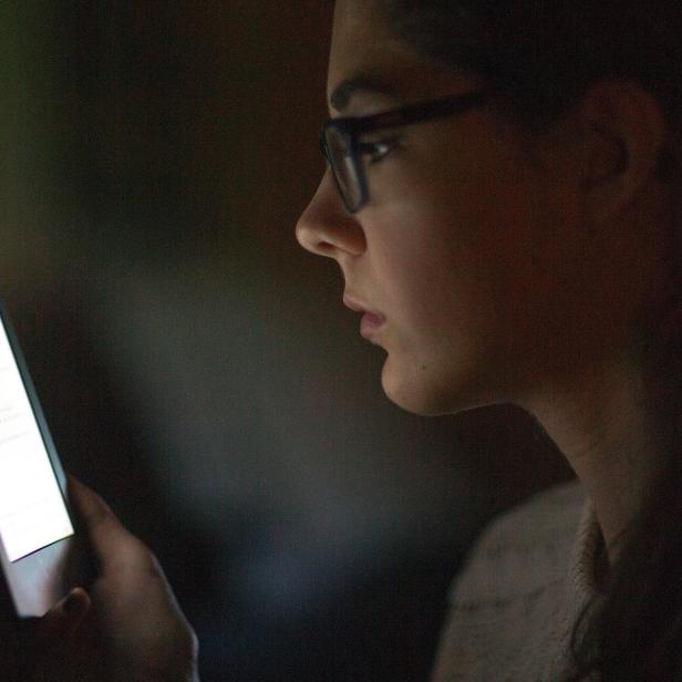 Eine Frau mit Brille liest auf einem E-Reader im Dunkeln.