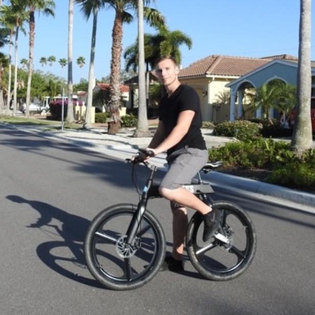 Ein Mann fährt ein dreirädriges Fahrrad auf einer Straße mit Palmen.