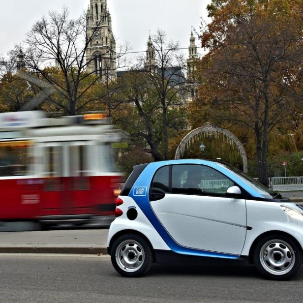 Ein weißer Smart steht am Straßenrand in Wien, während eine rote Straßenbahn vorbeifährt.