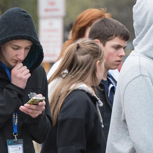Eine Gruppe junger Leute steht beieinander, ein Jugendlicher schaut auf sein Handy.