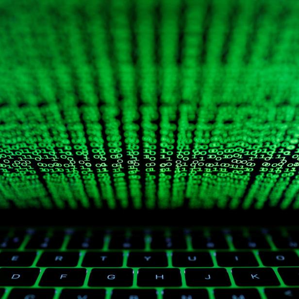 Ein Laptop-Bildschirm zeigt grünen binären Code vor einer beleuchteten Tastatur.