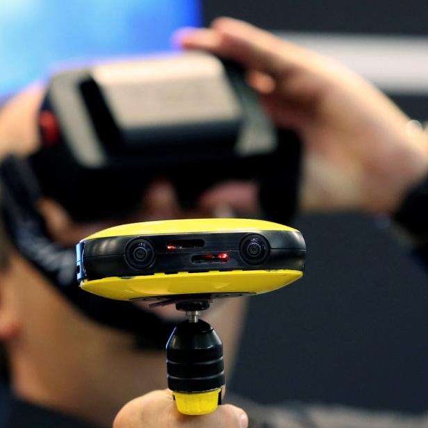 Eine Person trägt ein VR-Headset und hält eine gelbe 360-Grad-Kamera in der Hand.