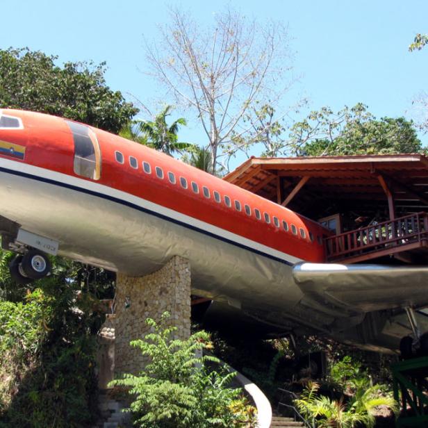 Ein rotes Flugzeug dient als ungewöhnliches Haus inmitten üppiger Vegetation.