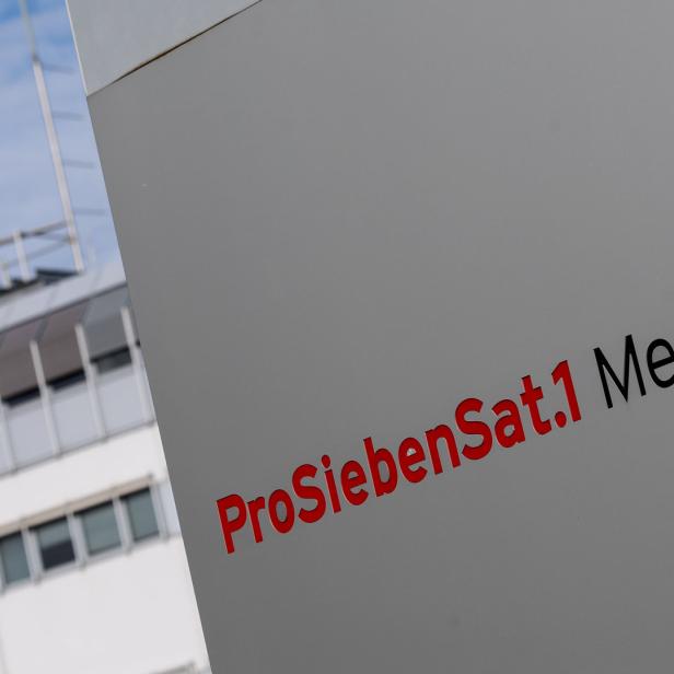 Das Logo von ProSiebenSat.1 Media SE vor einem Gebäude mit Satellitenschüssel.