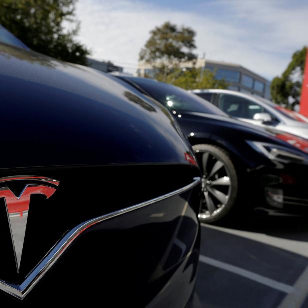 Mehrere Tesla-Fahrzeuge stehen vor einem Tesla-Schild.
