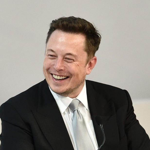 Elon Musk lächelt in einem schwarzen Anzug und einer silbernen Krawatte.