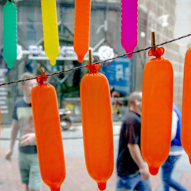 Mehrfarbige, gefüllte Ballons hängen an einer Wäscheleine vor einem Schaufenster.