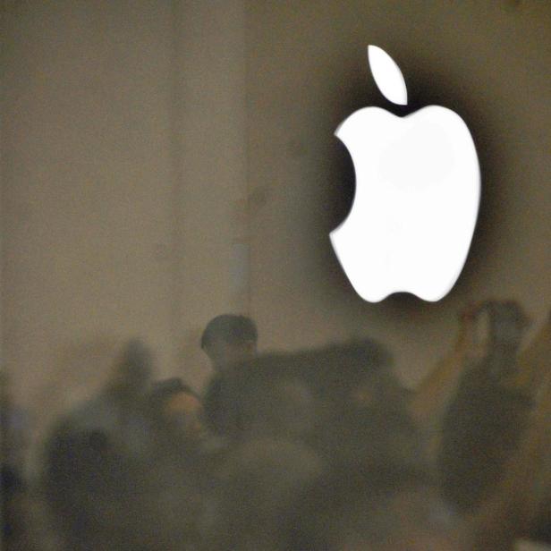 Das Apple-Logo leuchtet über einer Menschenmenge, die sich im Inneren eines Geschäfts spiegelt.