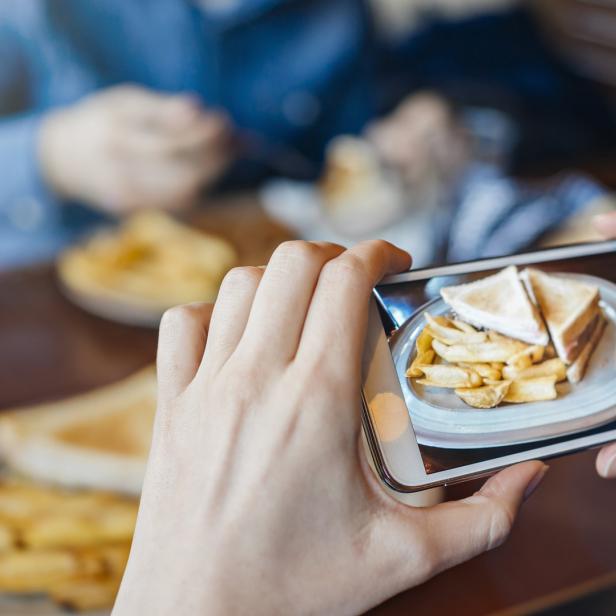 Eine Person fotografiert ein Sandwich mit Pommes Frites auf einem Teller.
