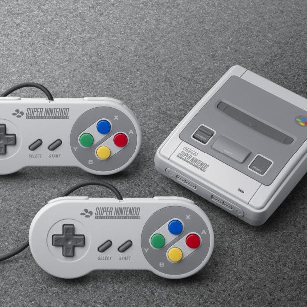 Ein Super Nintendo Entertainment System mit zwei Controllern auf einem grauen Untergrund.