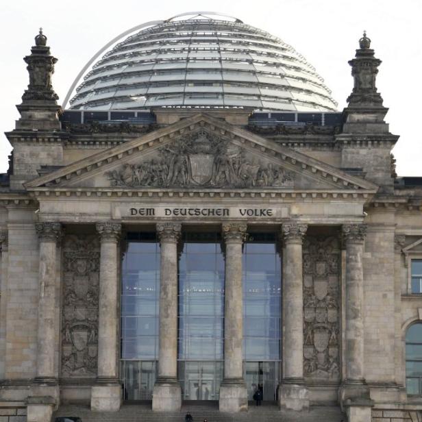 Der Reichstag in Berlin mit der deutschen Flagge im Vordergrund.