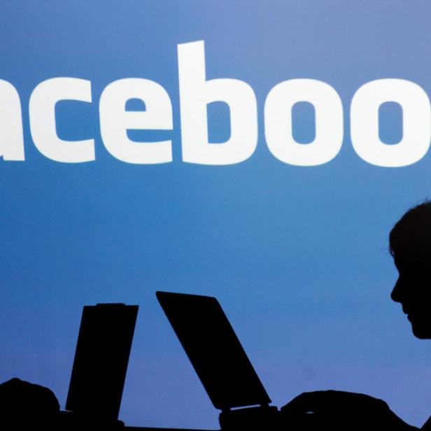 Zwei Personen arbeiten an Laptops vor einem Facebook-Logo.