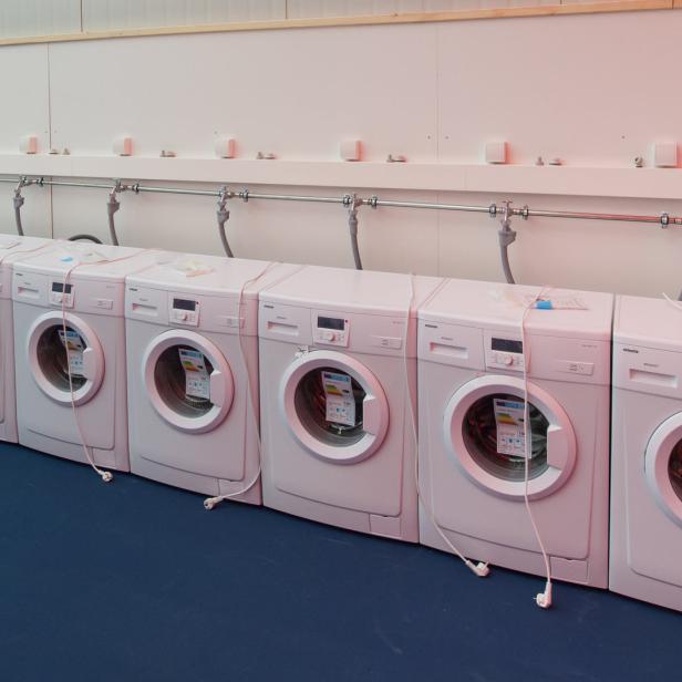 Eine Reihe von weißen Waschmaschinen steht an einer Wand.