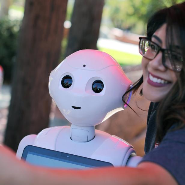 Eine Frau macht ein Selfie mit einem weißen Roboter.