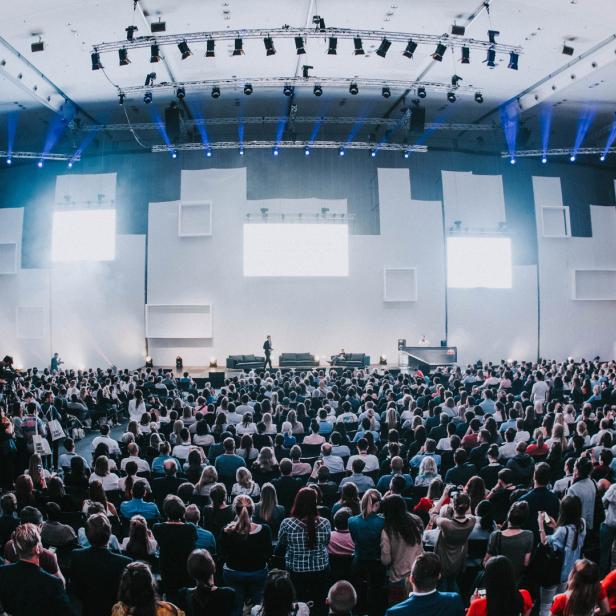 Ein großer Konferenzsaal mit vielen Zuhörern und einer Bühne mit Sofas.