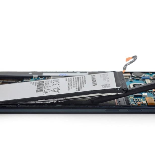 Ein Akku wird mit einem Werkzeug aus einem geöffneten Samsung-Smartphone entfernt.