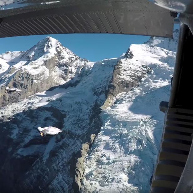 Blick aus einem Flugzeug auf schneebedeckte Berge und zwei Wingsuit-Springer.