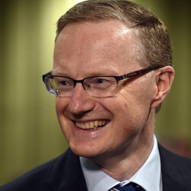 Ein lächelnder Mann mit Brille und Anzug vor einem grünen Hintergrund.