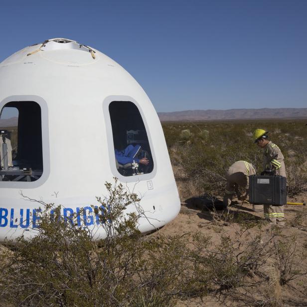 Eine Blue Origin Kapsel liegt in der Wüste, während Arbeiter sie inspizieren.
