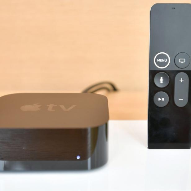 Ein Apple TV Gerät mit zugehöriger Fernbedienung auf einer weißen Oberfläche.