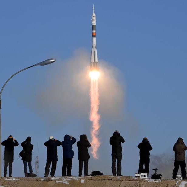 Eine Rakete startet vor blauem Himmel, beobachtet von einer Gruppe Menschen.