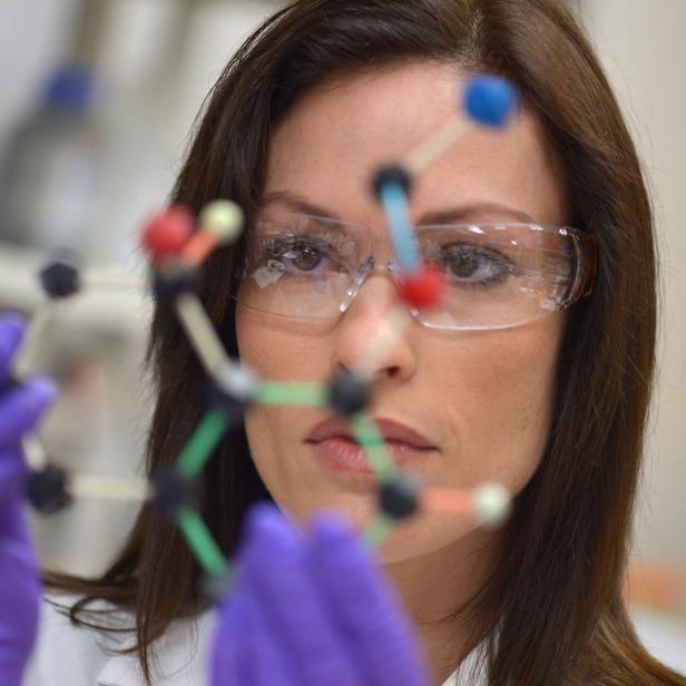 Eine Wissenschaftlerin mit Schutzbrille untersucht ein Molekülmodell im Labor.
