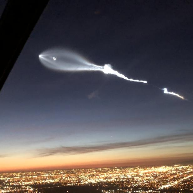 Eine Rakete steigt über einer beleuchteten Stadt in den Nachthimmel auf.