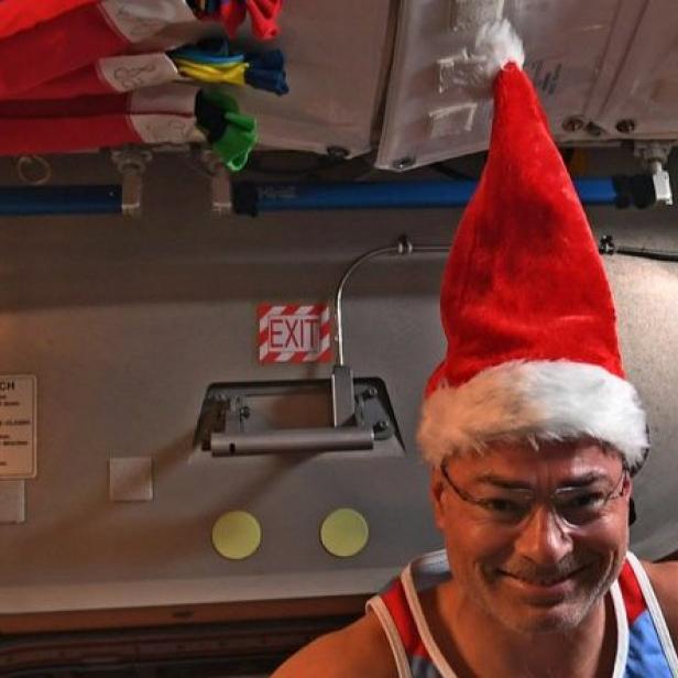 Ein Mann mit Brille und Weihnachtsmütze in einer Raumstation.