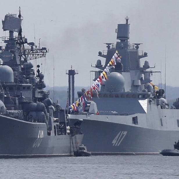 Zwei graue Kriegsschiffe liegen im Wasser, das eine geschmückt mit Flaggen.