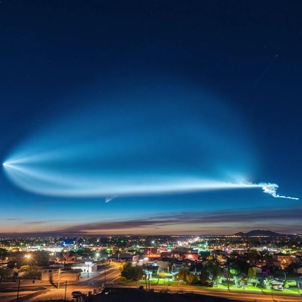 Der Nachthimmel über einer Stadt wird von den Lichtspuren einer Rakete erhellt.