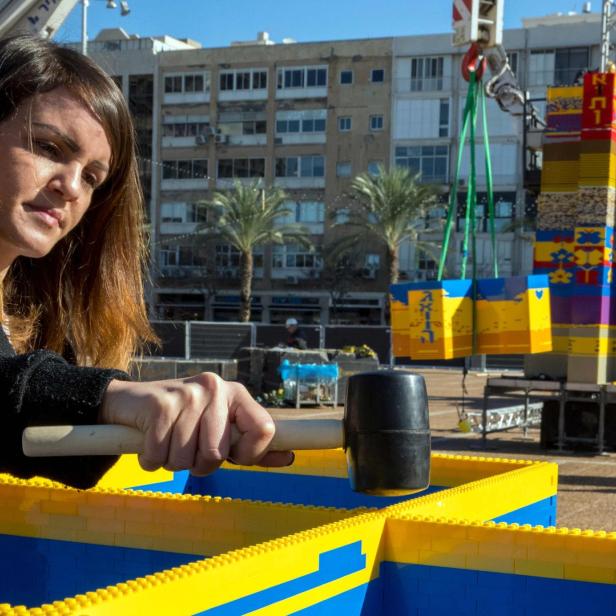 Eine Frau baut mit einem Hammer an einem Bauwerk aus Legosteinen.
