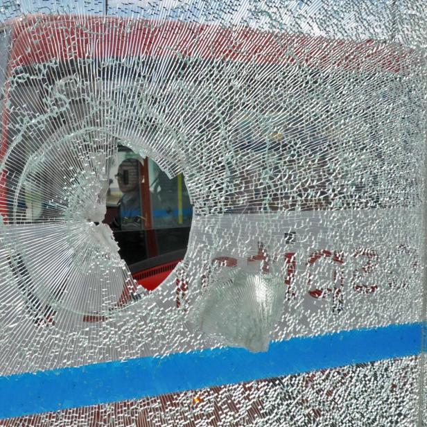 Eine zerbrochene Glasscheibe mit einem Loch, durch das ein roter Bus zu sehen ist.