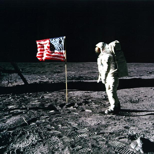 Ein Astronaut steht neben der US-amerikanischen Flagge auf der Mondoberfläche.