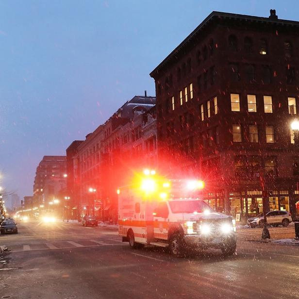Ein Krankenwagen fährt mit eingeschaltetem Blaulicht durch eine verschneite Stadt.