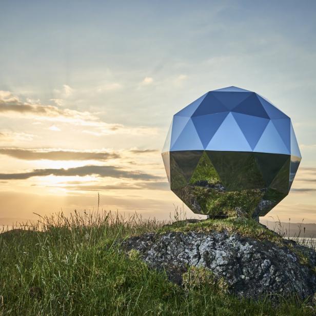 Eine geodätische Kuppel steht auf einem Felsen in einer grünen Landschaft bei Sonnenuntergang.