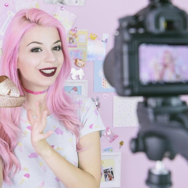 Eine Frau mit rosa Haaren präsentiert glitzernde Schuhe vor einer Kamera.