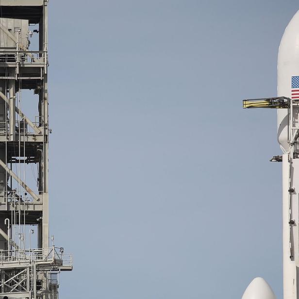 Eine Rakete mit amerikanischer Flagge steht auf einer Startrampe neben einem Versorgungsturm.